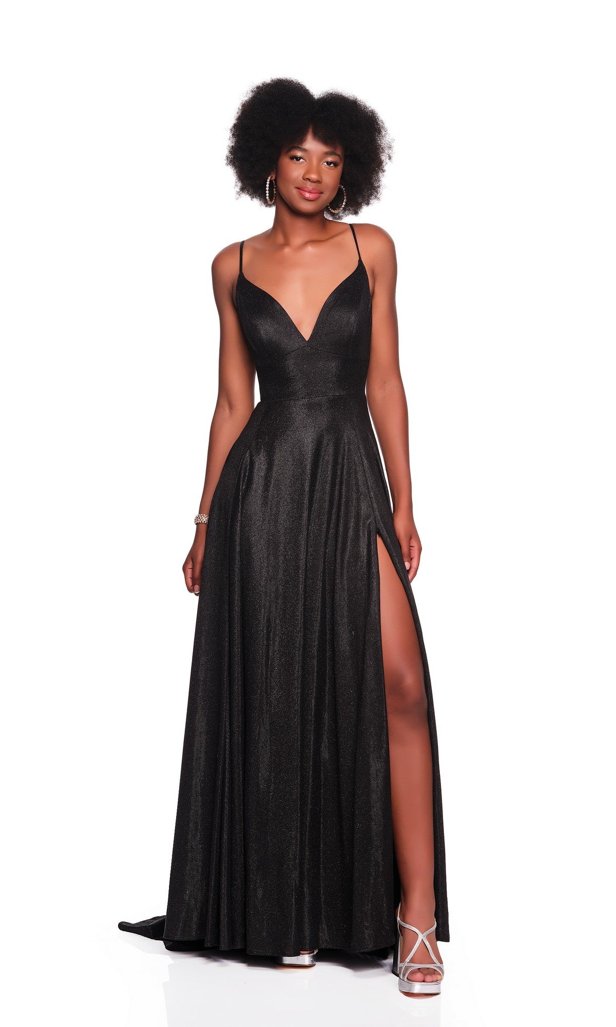 A woman wearing the Dave and Johnny 12408 long prom dress, featuring a sleeveless black design with a deep V-neck and high slit, pairs it with white strappy heels while standing against a white background.